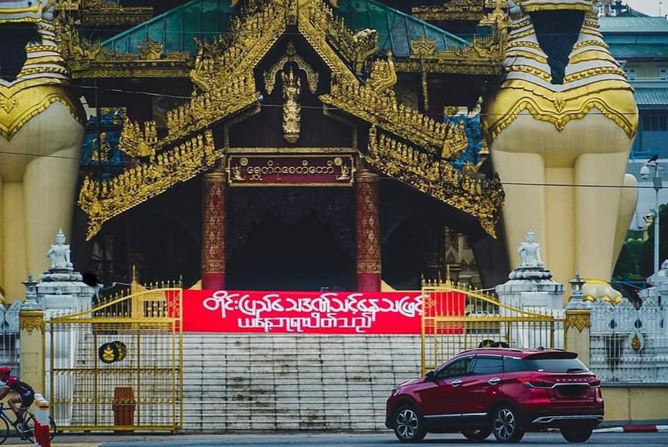 ရန်ကုန်မြို့ ရွှေတိဂုံစေတီတော်  တောင်ဘက်မုခ်ဦးဝမှာ  "တိုင်းပြည် သေဒဏ်သင့်နေသဖြင့် ယနေ့ ဘုရားပိတ်သည်" ဆိုသည့် စာတန်းချိတ်ဆွဲထားတာကို  ၂၀၂၂ ခုနှစ် ဇွန်လ ၁၃ ရက်နေ့မှာ တွေ့ရစဥ် (Photo: Yangon People's Strike)