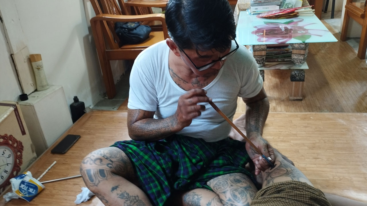 မန္တလေးမြို့မှ မြန်မာ့ရိုးရာဆေးမင်ကြောင်ဆရာ ဦးသက်နိုင် ဆေးမင်ကြောင်ထိုးပေးနေသည်ကို ၂၀၂၃ ခုနှစ်၊ ဇူလိုင်လ ၁၈ ရက်နေ့က တွေ့ရစဉ်။ (Photo: RFA)
