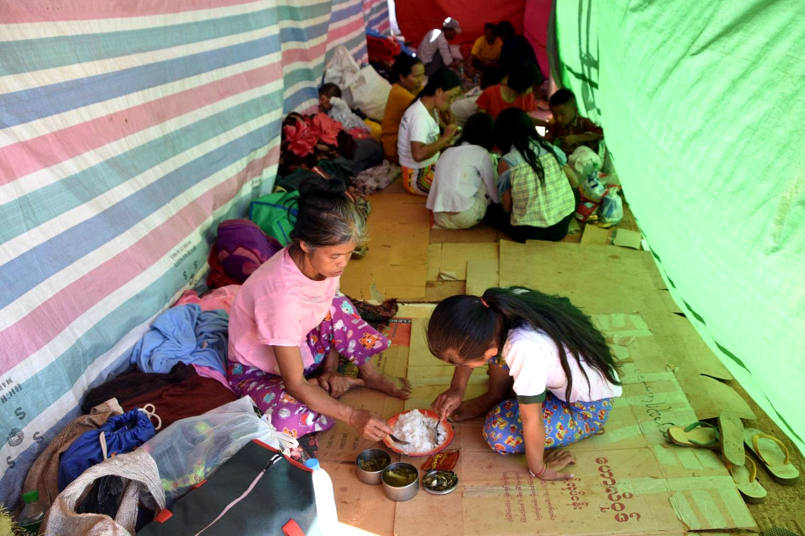 ယာယီတဲတန်းလျားများ မပြီးစီးခင် ဖြစ်သလို နေထိုင်စားသောက်နေရသည့် စစ်ပြေးဒုက္ခသည်များ။ (Photo: RFA)
