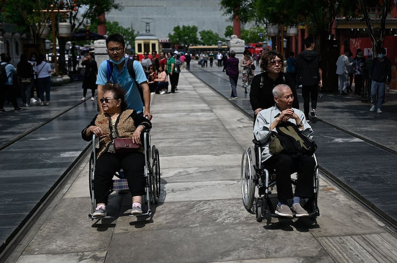 2021年5月11日,在北京的一条街道上,一对老年男女被推着坐在轮椅上。 (法新社)