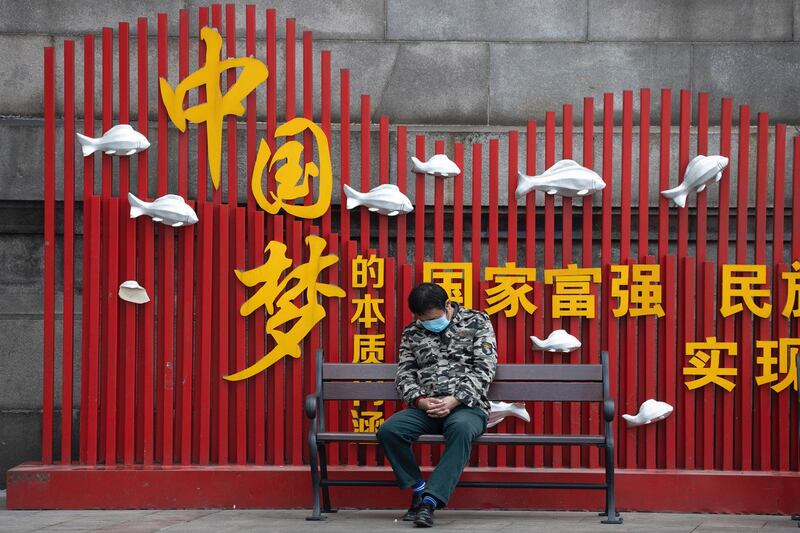 湖北武汉一名居民2020年4月1日在“中国梦”宣传标语前打盹( 美联社)