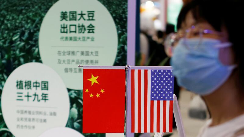 2021 年 9 月 4 日,北京举行的 2021 年中国国际服务贸易交易会(CIFTIS)期间,一名妇女走过美国大豆出口委员会展位上展示的中国和美国国旗。(路透社)