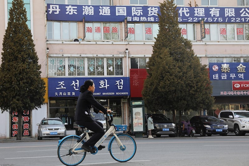资料图:一名妇女骑着脚踏车经过紧邻朝鲜的辽宁省丹东市区,路旁的招牌显示一家与朝鲜贸易的公司。(路透社资料图片)