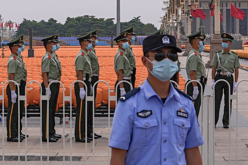 2021年6月28日,北京天安门广场上一排排座位旁,一名戴着口罩的警察在准备执勤的中国准军事人员旁边站岗。