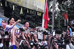 ၂၀၁၀ ခုနှစ် နိုဝင်ဘာလ ၁၃ ရက်နေ့ ညနေက ဒေါ်အောင်ဆန်းစုကြည် နေအိမ်အကျယ်ချုပ်မှ လွတ်မြောက်လာပြီးနောက် ကြိုဆိုနေသူများကို နေအိမ်ခြံတံခါးမှ လက်ဝှေ့ရမ်း နှုတ်ဆက်နေစဉ်။ (Photo: AFP)