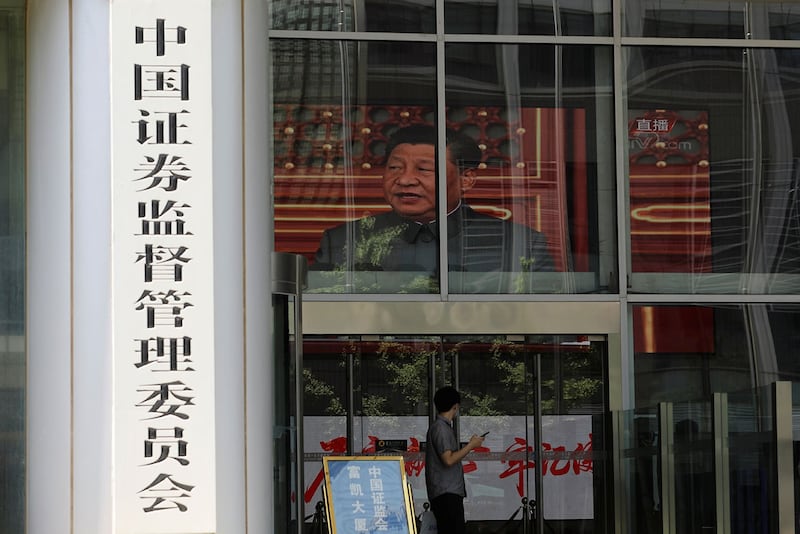 资料图片:2021 年 7 月 9 日,一名男子站在中国证券监督管理委员会大楼的屏幕附近,播放习近平的新闻镜头。(路透社)